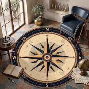 Könnte beinhalten: Ein runder Teppich mit einem Kompassrosen-Design. Der Teppich hat einen cremefarbenen Hintergrund mit einem marineblauen Rand und Kompasspunkten. Die Kompassrose hat goldene und marineblaue Akzente, mit den Himmelsrichtungen.