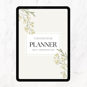 Puede incluir: Un planificador digital en una tableta con las palabras "UNDATED YEAR PLANNER DAILY ORGANISATION". El planificador tiene un fondo color crema con detalles florales y un borde negro.