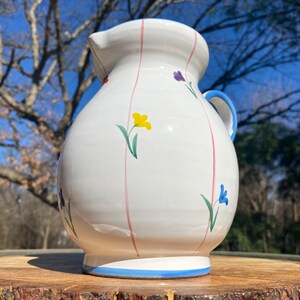 May include: White ceramic pitcher with pink and blue stripes and floral designs in yellow, blue, and purple.