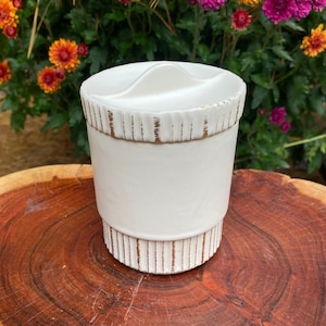 May include: White ceramic jar with a gold rim and a gold stripe design. The jar has a lid with a small opening.