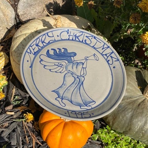 May include: A ceramic plate featuring a blue and white design of an angel playing a trumpet. The plate reads "Merry Christmas" and "1995".