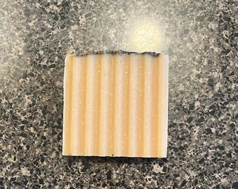 Op de afbeelding: Een rechthoekige zeep met een lichtoranje kleur en een getextureerd oppervlak. De zeep heeft een lichtbruin streepdessin.