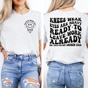 May include: Light gray t-shirt with a smiley face graphic and the text "WHATEVER EMINEM SAID" on the front. The back of the shirt features the text "KNEES WEAK EYES ARE HEAVY READY TO LEAVE WORK ALREADY OR WHATEVER EMINEM SAID."