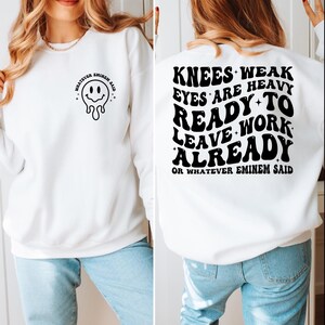 May include: White sweatshirt with black text and a melting smiley face graphic. The front of the sweatshirt says "WHATEVER EMINEM SAID" with a melting smiley face. The back of the sweatshirt says "KNEES WEAK EYES ARE HEAVY READY TO LEAVE WORK ALREADY OR WHATEVER EMINEM SAID."