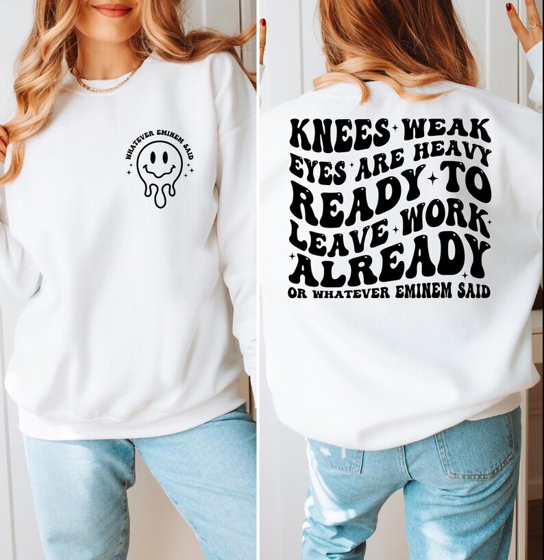 May include: White sweatshirt with black text and a melting smiley face graphic. The front of the sweatshirt says "WHATEVER EMINEM SAID" with a melting smiley face. The back of the sweatshirt says "KNEES WEAK EYES ARE HEAVY READY TO LEAVE WORK ALREADY OR WHATEVER EMINEM SAID."