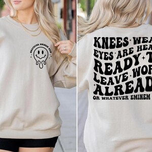 May include: Beige sweatshirt with a black smiley face graphic and the text "WHATEVER EMINEM SAID" on the front. The back features the text "KNEES WEAK EYES ARE HEAVY READY TO WORK LEAVE ALREADY OR WHATEVER EMINEM SAID" in black.