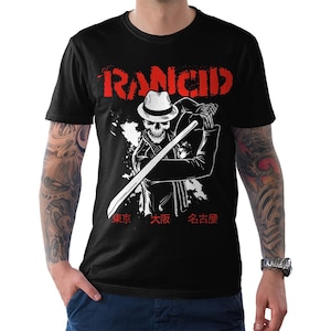 Puede incluir: Camiseta negra con un gráfico blanco de un esqueleto con un sombrero y sosteniendo una espada. El texto "Rancid" está en rojo sobre el gráfico y el texto "東京 大阪 名古屋" está en rojo debajo del gráfico.