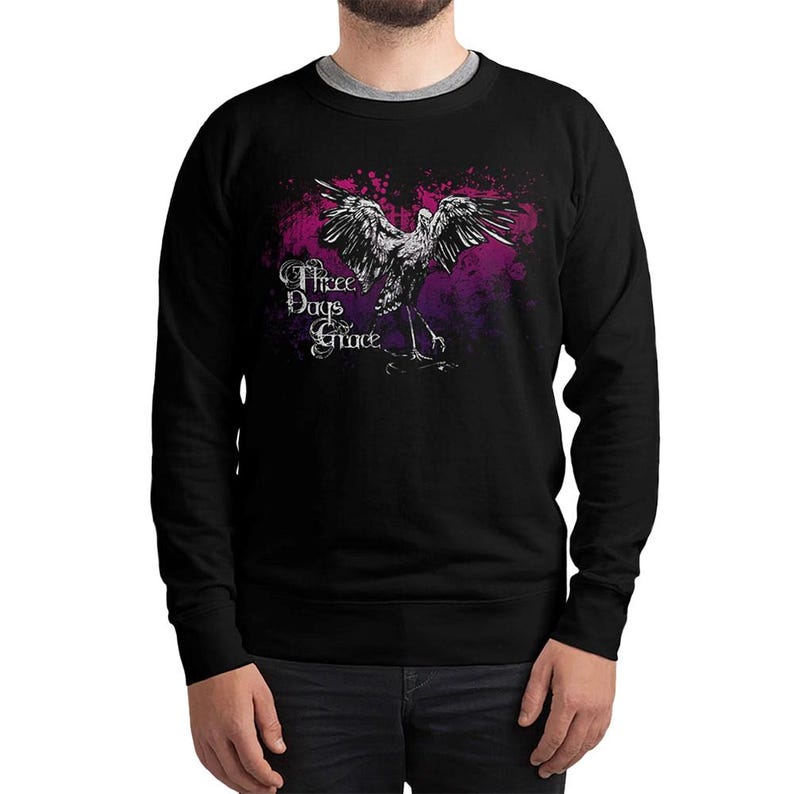 May include: Black crew neck sweatshirt featuring a graphic of a bird with outstretched wings, set against a purple and pink splatter design. The text "Three Days Grace" is printed in white script. A casual, comfortable apparel item.