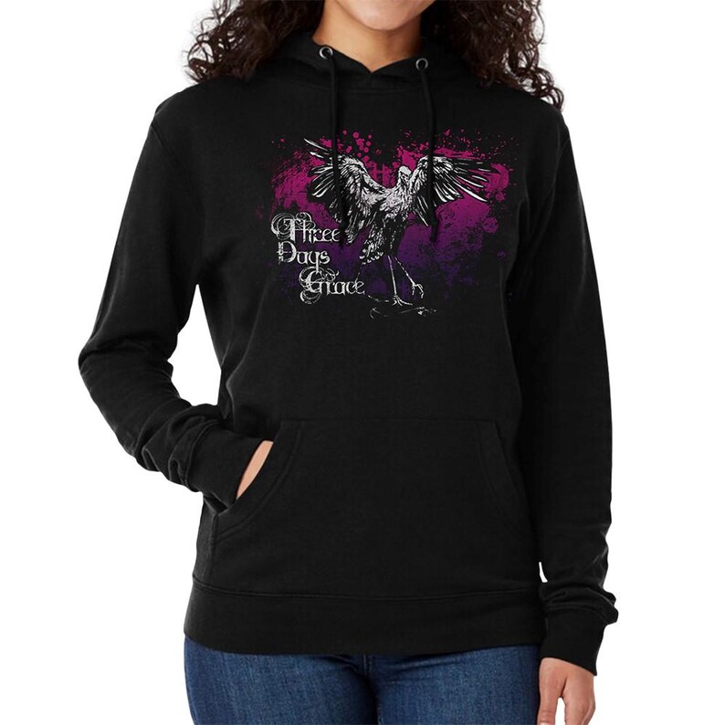 May include: Black hooded sweatshirt featuring a graphic of a bird with outstretched wings, set against a purple and pink splatter design. The text "Three Days Grace" is printed in white script. The sweatshirt has a front pocket.