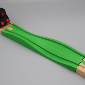 Könnte beinhalten: Eine grüne Holz-Eisenbahnstrecke mit einem gebogenen Abschnitt. Ein roter Spielzeugzug befindet sich auf der Strecke.
