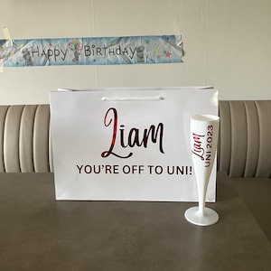 May include: White gift bag with red lettering that says "Liam You're Off To Uni!" and a white champagne flute with red lettering that says "Liam Uni 2023".
