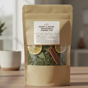 May include: A brown paper bag with a clear window displaying a simmer pot blend. The label reads "Heart's Desire Abundance Simmer Pot" with text below. The blend includes lemon slices, bay leaves, cinnamon sticks, and dried herbs. The bag is on a wooden surface.