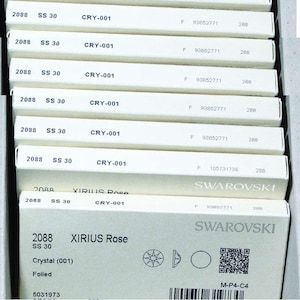 Puede incluir: Primer plano de una caja blanca con el texto "XIRIUS Rose" y "SS 30" impreso en ella. La caja también incluye un pequeño cristal transparente con un diseño en forma de estrella. El texto "SWAROVSKI" está impreso en la esquina inferior derecha de la caja.