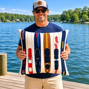 May include: A rectangular cushion with a design of water skis in red, blue, and brown. The skis are set against a cream background with vertical stripes. The cushion is held by a person wearing sunglasses and a baseball cap.