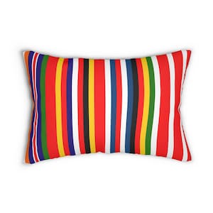 Puede incluir: Cojín rectangular con un vibrante diseño de rayas. El diseño presenta rayas verticales en varios colores, incluyendo rojo, blanco, azul, amarillo y negro. La almohada tiene una apariencia suave y afelpada, lo que sugiere comodidad y uso decorativo.