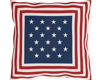 Könnte beinhalten: Quadratisches Kissen mit patriotischem Design. Das Kissen hat eine marineblaue Mitte mit weißen Sternen, die von einem rot-weiß gestreiften Rand umgeben ist. Das Design erinnert an die amerikanische Flagge.