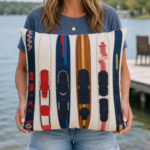 May include: Cream cushion with a pattern of vintage water skis in various colours. The skis are mainly blue, red, and brown, with black bindings. The cushion has a nautical or lake house theme.