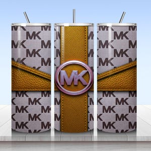 May include: A cylindrical tumbler with a straw featuring a repeating MK logo pattern on a light gray background. A textured mustard yellow band wraps around the center, accented by a circular emblem with the letters MK in a metallic purple finish.