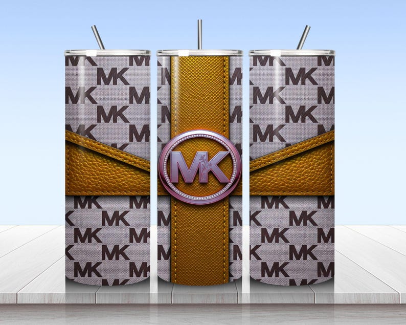 May include: A cylindrical tumbler with a straw featuring a repeating MK logo pattern on a light gray background. A textured mustard yellow band wraps around the center, accented by a circular emblem with the letters MK in a metallic purple finish.