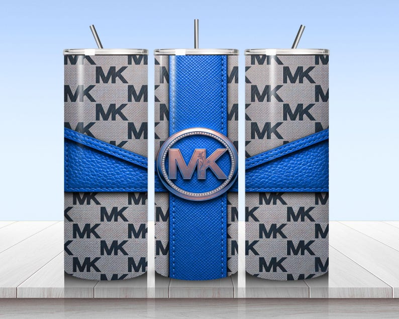May include: A cylindrical tumbler with a straw featuring a gray and black repeating MK logo pattern. A bright blue textured band wraps horizontally around the center, intersected by a vertical blue stripe with a circular MK logo emblem in the middle.