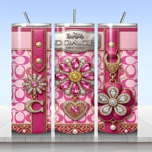 May include: A cylindrical tumbler with a pink and light pink repeating C logo pattern. The design features a vertical pink leather-textured strap, a silver Coach New York logo, and decorative floral charms adorned with pink and clear crystals.