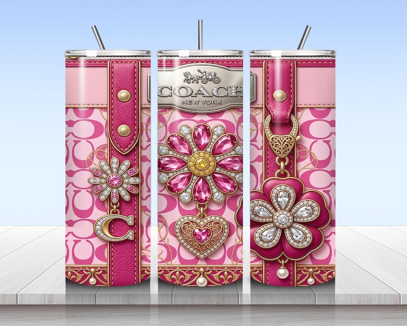 May include: A cylindrical tumbler with a pink and light pink repeating C logo pattern. The design features a vertical pink leather-textured strap, a silver Coach New York logo, and decorative floral charms adorned with pink and clear crystals.