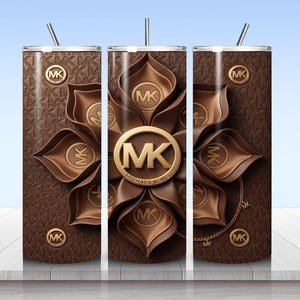 May include: A cylindrical tumbler with a straw, featuring a brown background with a repeating MK logo pattern. The design includes a large, central, layered brown flower graphic with a gold MK logo emblem and smaller gold MK logo accents throughout.