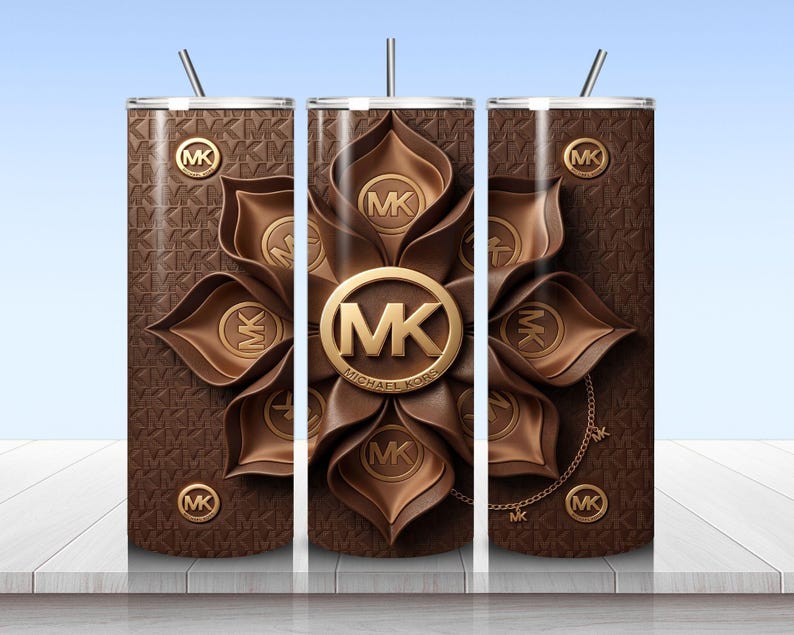 May include: A cylindrical tumbler with a straw, featuring a brown background with a repeating MK logo pattern. The design includes a large, central, layered brown flower graphic with a gold MK logo emblem and smaller gold MK logo accents throughout.