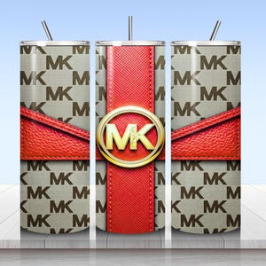 May include: A cylindrical tumbler with a straw featuring a beige and brown repeating MK logo pattern. A textured red band wraps horizontally around the center, intersected by a vertical red stripe and a gold circular emblem with the letters MK.