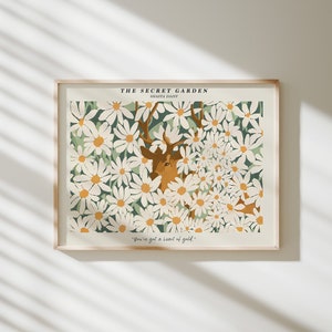 May include: A framed print with a white background featuring a stylized illustration of a deer surrounded by white daisies with green leaves. The text "THE SECRET GARDEN" and "SHANTA DAIRY" are at the top of the print. The text "You've got a heart of gold." is at the bottom of the print.