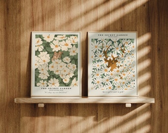 Puede incluir: Dos impresiones enmarcadas con diseños florales y texto. La impresión de la izquierda presenta una ardilla en un campo de flores blancas con hojas verdes. El texto dice "The Secret Garden" y "He is always my very best friend". La impresión de la derecha presenta un ciervo en un campo de flores blancas con hojas verdes. El texto dice "The Secret Garden" y "You're got a land of your own".