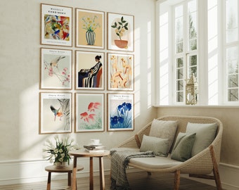 May include: A living room with a white sofa and a wall decorated with framed art prints. The prints feature a variety of subjects, including birds, flowers, and abstract designs. The prints are arranged in a grid pattern on the wall. The sofa is made of wicker and has a white cushion. There is a small table in front of the sofa with a cup and saucer on it.