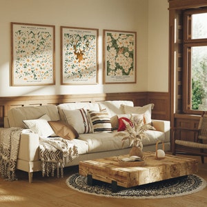 May include: A living room interior with a white couch, a wooden coffee table, and three framed prints of floral illustrations with the text "The Secret Garden". The prints are hung on a white wall above a wooden wainscot.