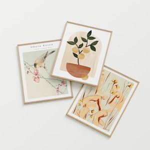 May include: Three framed art prints with neutral tones. One print features a bird perched on a flowering branch, another depicts a plant with fruit, and the third showcases abstract figures among flowers. The frames are light brown.