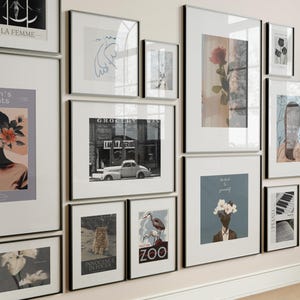 May include: A collection of framed art prints in various sizes and styles. The images include a black and white photograph of a vintage car, a rose, and abstract illustrations. Some prints have text, including "LA FEMME" and "ZOO".