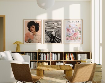 May include: A living room scene featuring three framed art prints. The prints depict a portrait, a black and white expressionist image, and a floral design with the text "FLEURS GARDEN BLOOM". The room includes a white sofa, wooden furniture, and two woven chairs.
