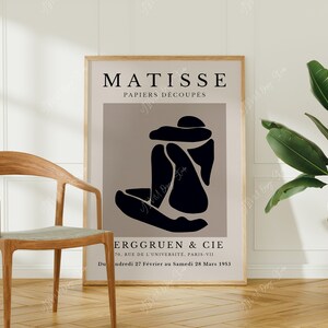 May include: A black and white poster with the text "MATISSE PAPIERS D&Eacute;COUPES" and a black abstract figure on a light brown background. The poster also includes the text "ERGGRUEN & CIE 70, RUE DE L'UNIVERSITE, PARIS-VII Du ndredi 27 F&eacute;vrier au Samedi 28 Mars 1953".