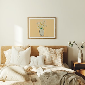 May include: A white bed with a striped beige and white throw pillow and a white pillow. The bed has a beige and white striped duvet cover and a beige throw blanket. There is a framed print of a vase of white flowers on the wall behind the bed.