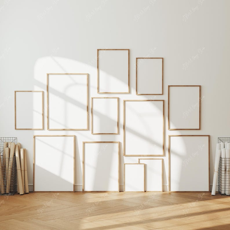 May include: A collection of framed art prints in various sizes, arranged on a white wall. The frames are a light wood color, and the prints are blank, ready for artwork or photos. The room has a wooden floor and is well-lit.