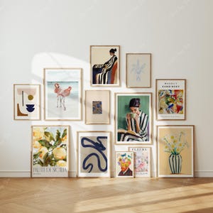 May include: A gallery wall arrangement featuring framed art prints. The collection includes abstract designs, flamingo beach scene, a portrait of a person, floral and fruit illustrations, and a Wassily Kandinsky painting. The frames are in a natural wood tone.