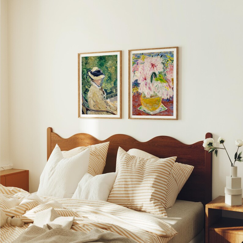 May include: Two framed paintings hanging on a white wall above a bed with a wooden headboard. The painting on the left shows a woman in a hat sitting in a chair outdoors. The painting on the right shows a bouquet of pink flowers in a yellow vase.