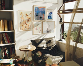 May include: A cozy living room corner with a black leather armchair, a small side table, and a bookshelf filled with books. The wall is decorated with framed artwork featuring a sailboat, a floral design, and a landscape scene.