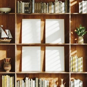 May include: A wooden bookcase with four empty picture frames, books, and decorative items. The bookcase is made of light brown wood and has a rustic look. The frames are all the same size and are arranged in a grid pattern. The books are stacked on the shelves and are of various sizes and colours. The decorative items include a small sailboat, a vase, and a potted plant.