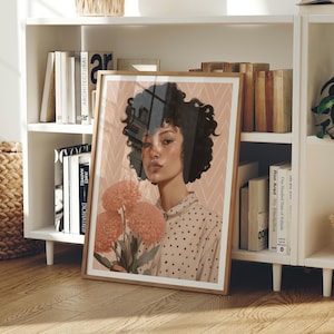 Puede incluir: Una impresión artística enmarcada que presenta un retrato de una persona con cabello rizado sosteniendo flores de color melocotón. La persona lleva una camisa de lunares. El fondo tiene un patrón geométrico rosa y blanco. El marco es de color marrón claro.