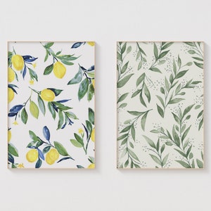 May include: Two framed prints with watercolor designs. The first print features a white background with yellow lemons and blue-green leaves. The second print features a light green background with dark green leaves.