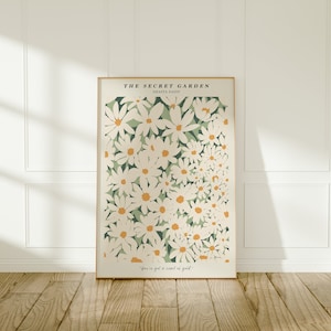 May include: A framed print with a white background and a floral pattern of white daisies with yellow centers on a green background. The text "THE SECRET GARDEN" and "SHASTA DAISY" is at the top of the print. The text "You've got a secret garden." is at the bottom of the print.