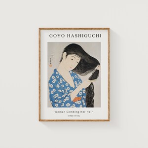 May include: A framed print of a woodblock print by artist Goyo Hashiguchi. The print depicts a woman in a blue and white patterned kimono combing her long black hair. The title of the print is "Woman Combing Her Hair (1900-1945)".