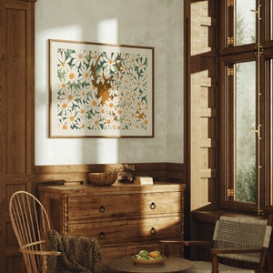 Könnte beinhalten: Ein gerahmter Druck eines weißen Gänseblümchen-Blumenmusters mit einer braunen Hirsch-Silhouette in der Mitte. Der Druck hängt an einer Wand in einem Raum mit Holzvertäfelung und einer Kommode aus Holz.