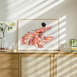 May include: A framed print of a watercolor painting depicting a woman wearing a red and white striped dress. The woman is lying on her back with her arms outstretched. The background is a light gray.