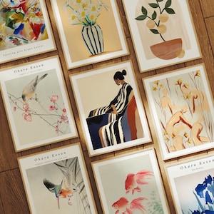 Puede incluir: Una colección de impresiones de arte enmarcadas que presentan varios estilos y temas, incluyendo pinturas abstractas, arreglos florales y diseños minimalistas. Las impresiones se muestran en una superficie de madera.